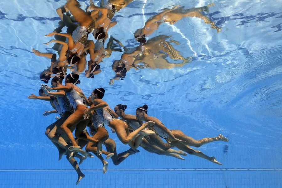 A team of artistic swimmers gathers just below the surface of a pool.