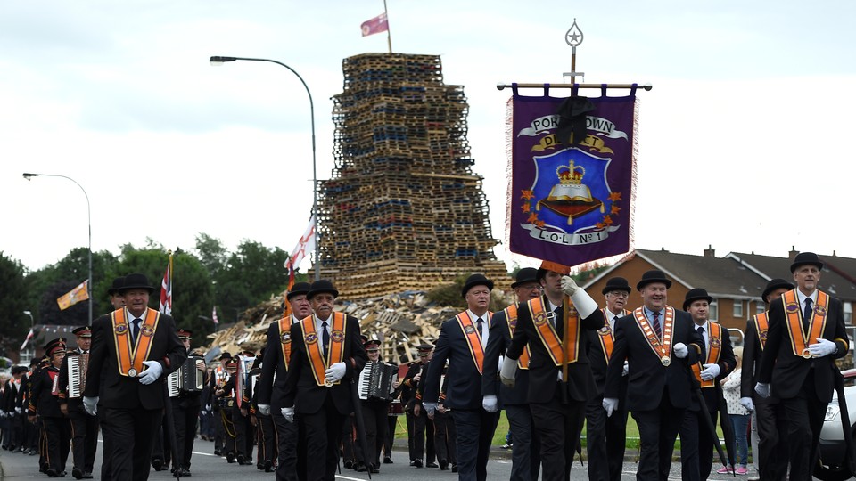 Participants in an Orange Order parade march past a bonfire pyre in Portadown, Northern Ireland.