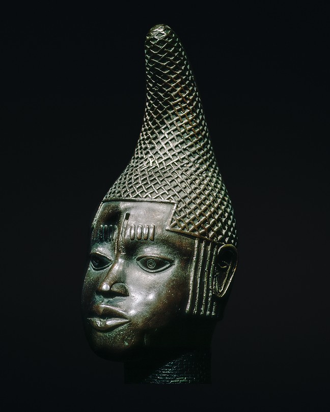 photo of a sculpture of a head with detailed conical headdress on black background