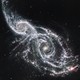 Two spiral galaxies take up almost the entire view and appear to be overlapping. The background of space is black, dotted with tiny foreground stars and extremely distant galaxies.