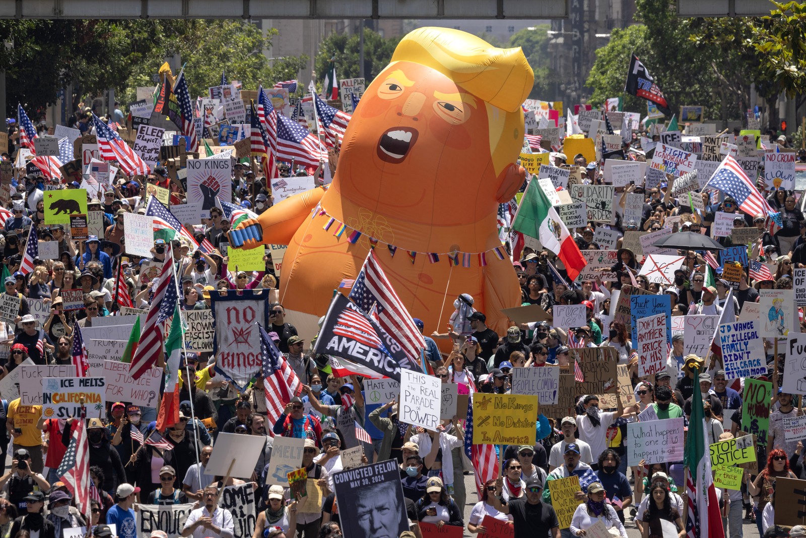A group of protesters marches down a street with a large inflatable caricature of Donald Trump being carried in their midst.