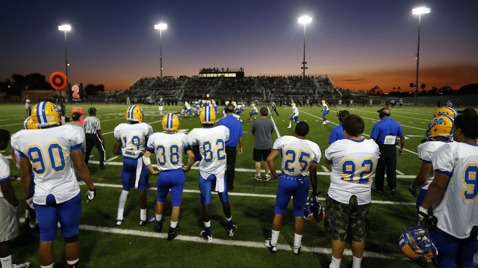 High-school football players look out onto the field as a game is played under the lights.