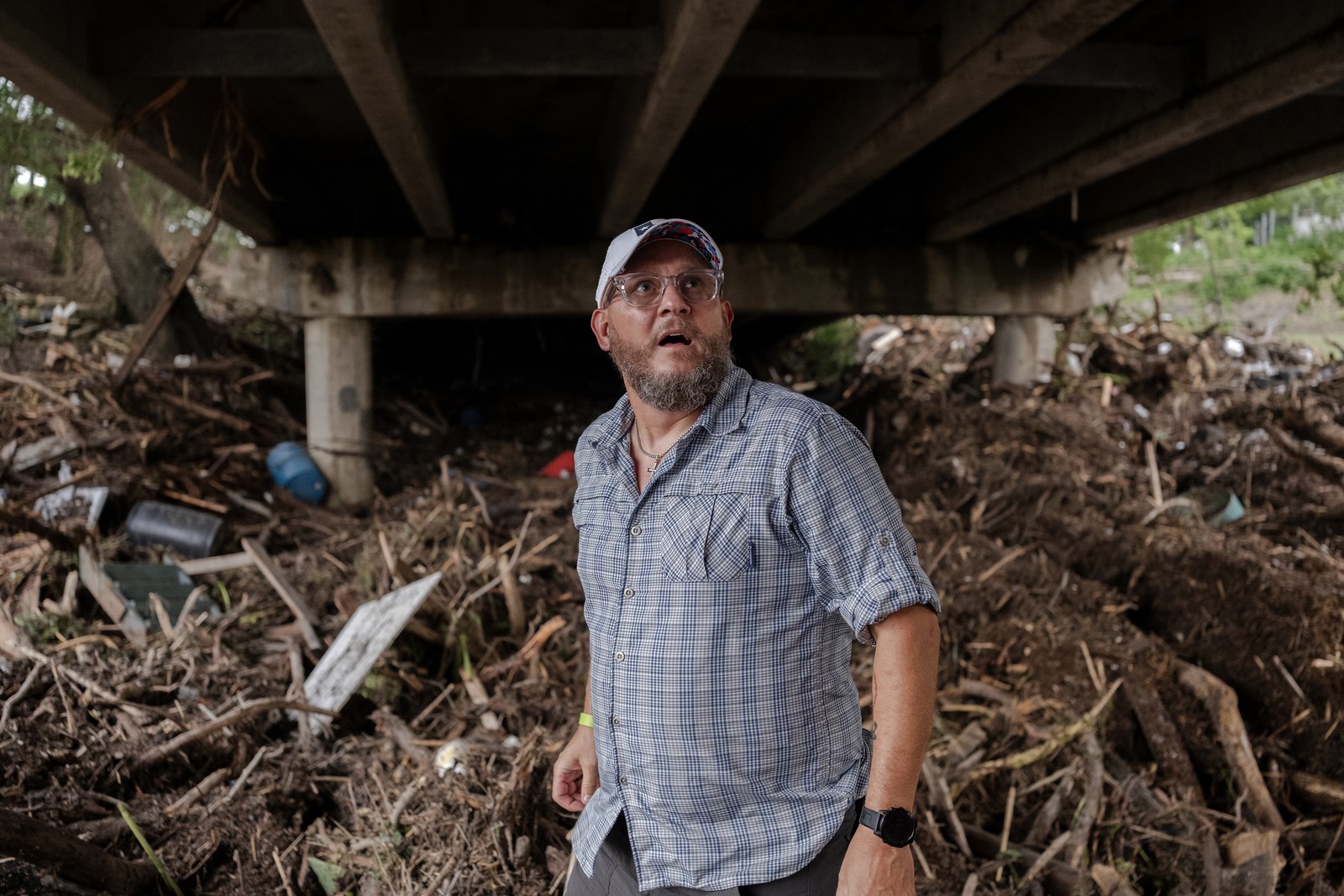 A person walks beneath a road bridge, with huge piles of flood debris visible behind them.