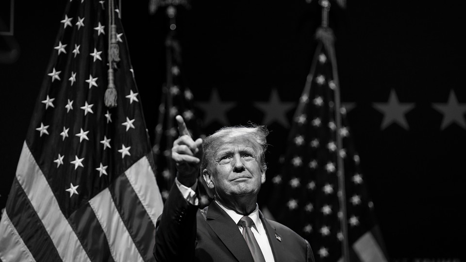 Black-and-white photograph of Donald Trump in front of some American flags