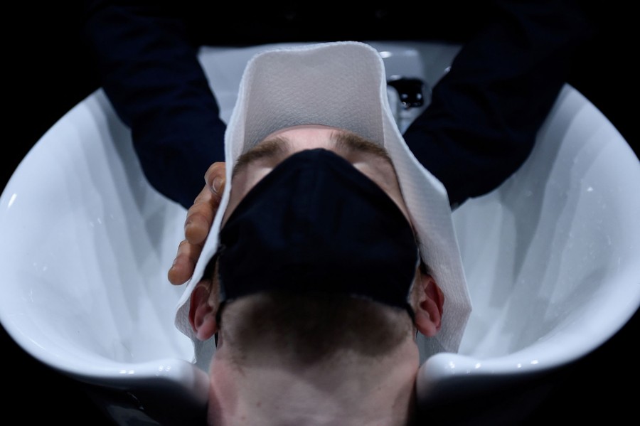 A masked man lies back as a hairdresser washes his hair.