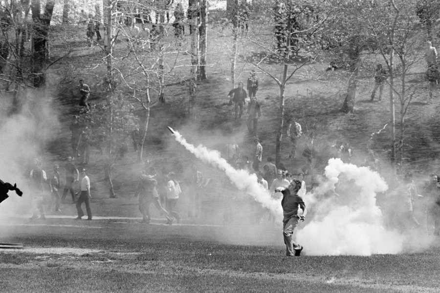 A person throws a tear-gas canister back toward National Guardsmen.