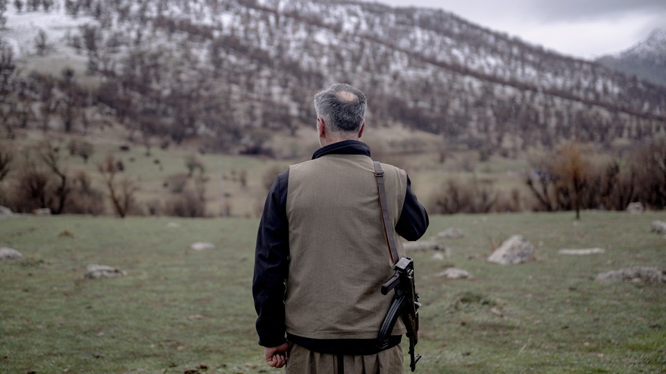 A man stands with his rifle, facing a mountain range.
