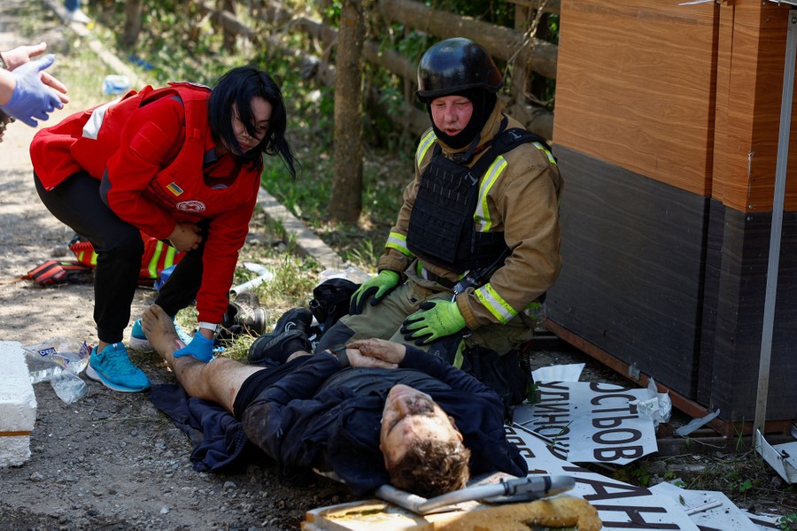 Two rescue workers kneel down to attend to a wounded man lying on the ground.