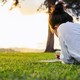 rear view of woman with black hair in a bun lying on her stomach on green grass, writing in a noteboo