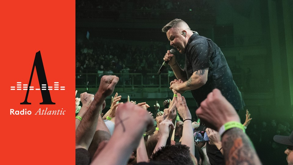 Ken Casey, front man of the Dropkick Murphys holds a microphone up to his mouth while reaching into the crowd at a concert