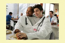 Donald Faison and Zach Braff sharing a single shirt and doctor's jacket, in a scene from "Scrubs"