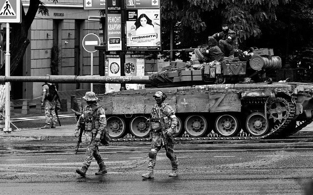 A black-and-white image shoes Wagner mercenaries walking next to a tank on a street in Rostov-on-Don.