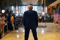 Trump stands, turned from the camera, hunched in front of a crowd of reporters