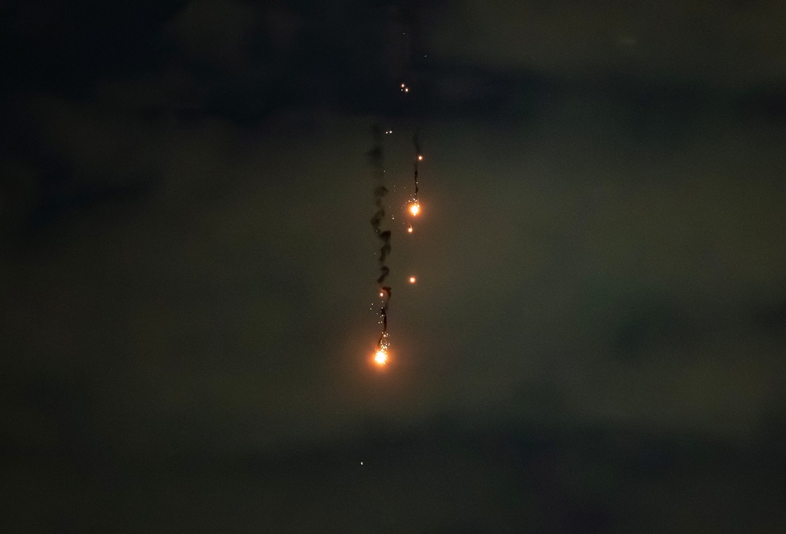 Flaming chunks of debris fall from the night sky, leaving dark trails of smoke.