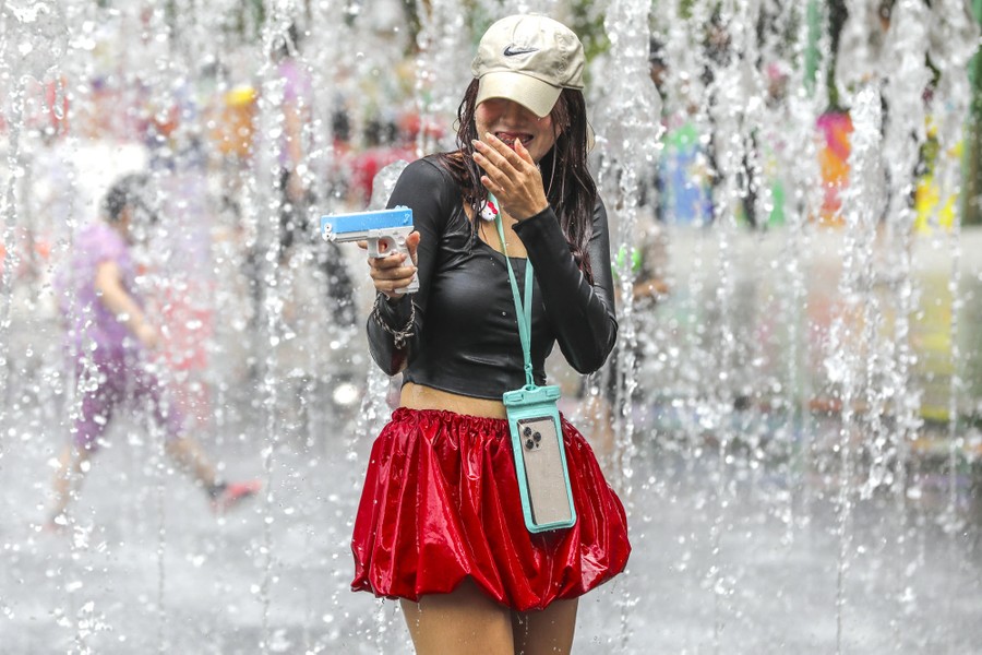 A person laughs near a water fountain, holding a water pistol.