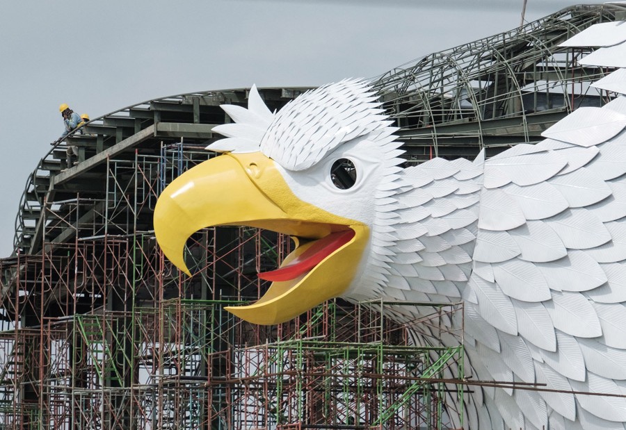 A closer view of a multistory building, under construction, with a large sculpture of a bird of prey