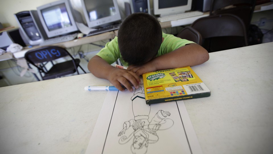 A child rests his head on the table next to a box of markers and a coloring page.