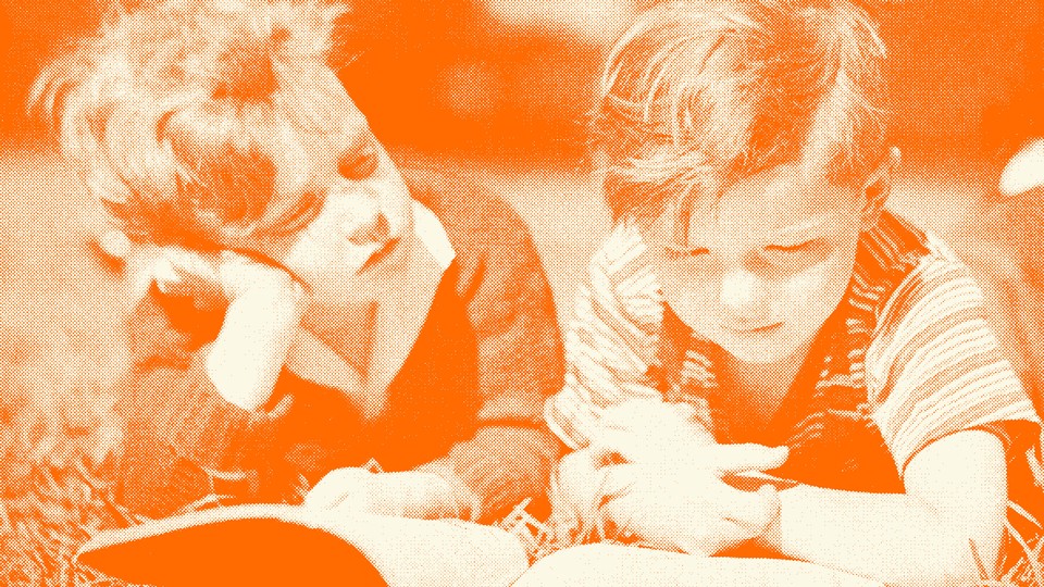 Two kids read a book together in the grass