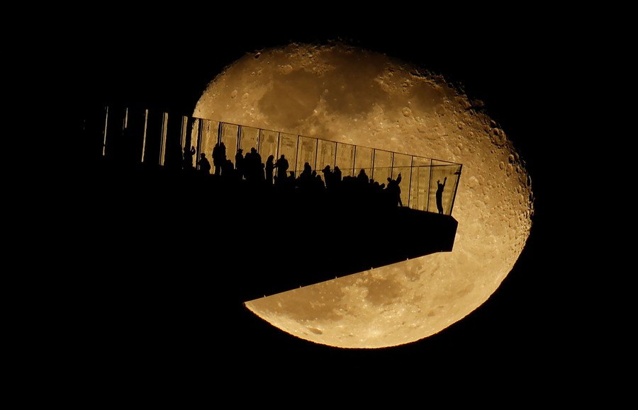 The moon rises behind a distant overhanging observation deck.