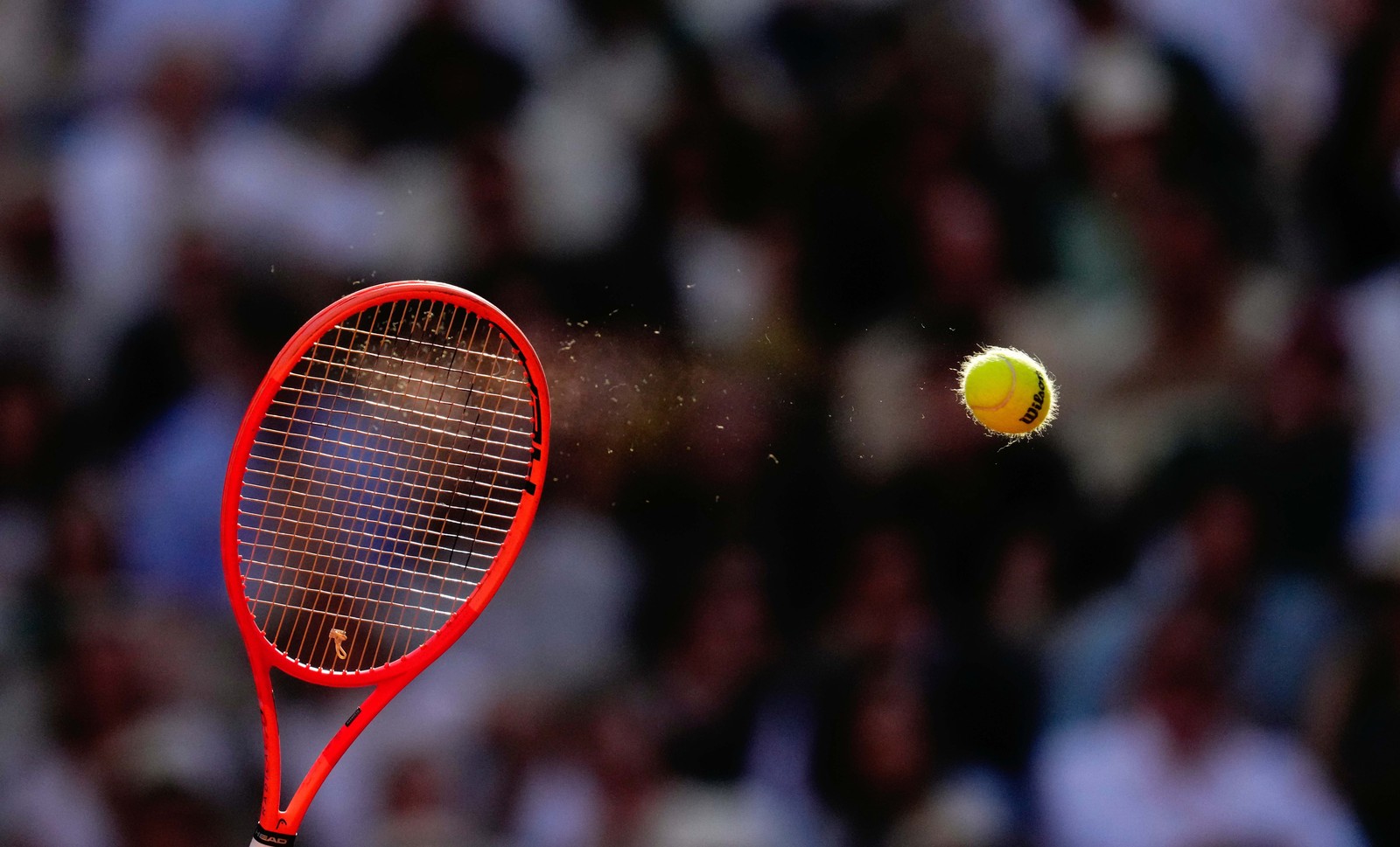 A tennis ball, looking slightly flattened, flies quickly away from a tennis racket after being struck.