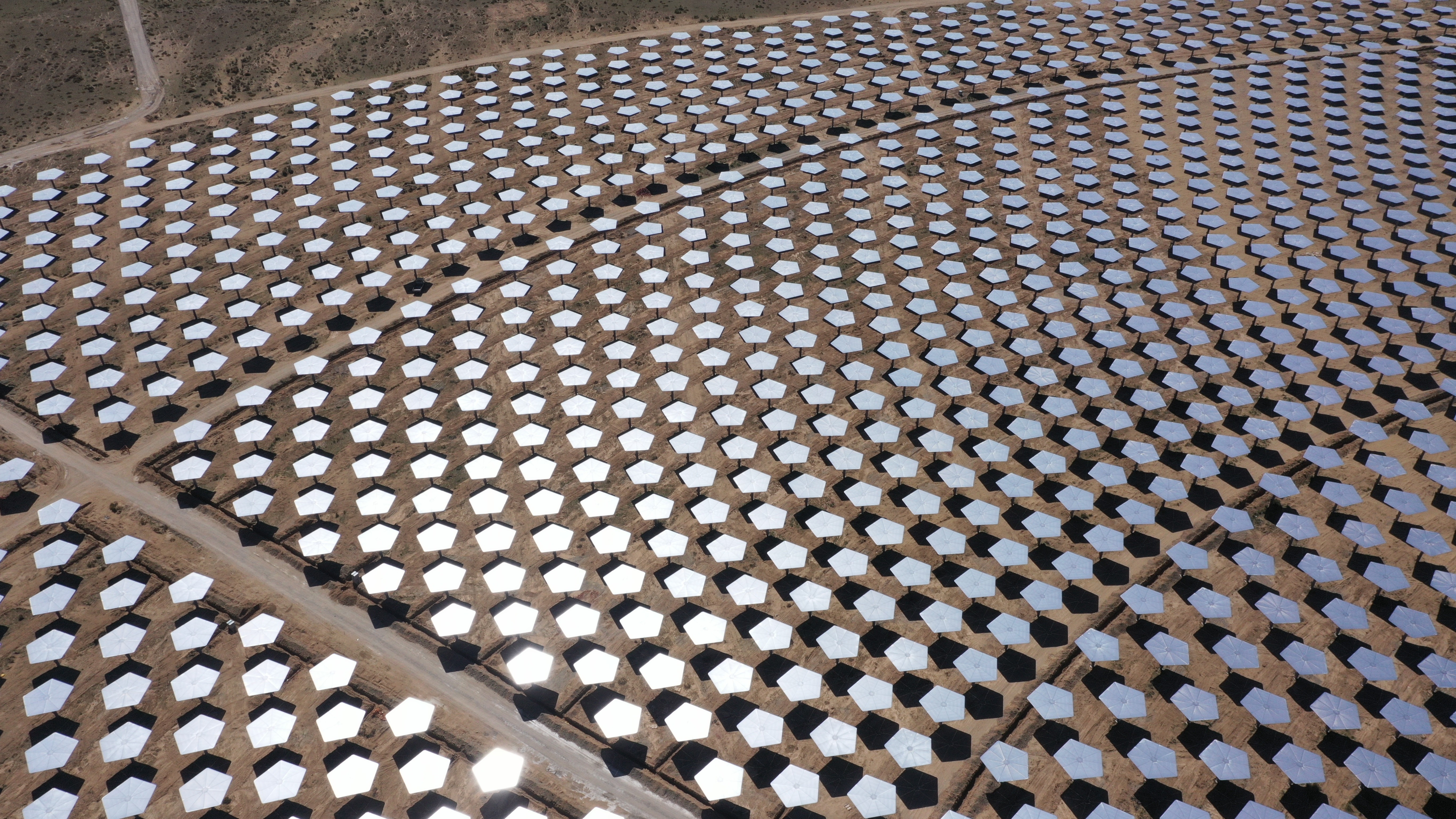 An aerial view of pentagon-shaped mirror panels arranged in a semi-circular pattern ina desert.