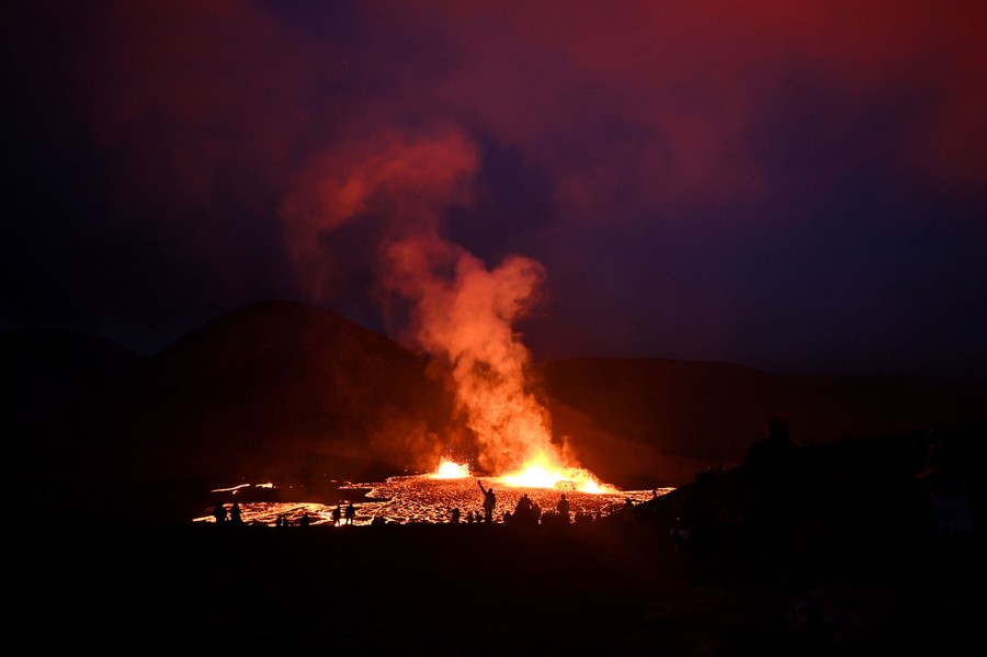 People are seen in silhouette at night in front of a lava flow.