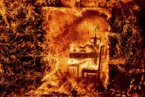 A view of the interior of a house, seen from outside, completely engulfed in fire.