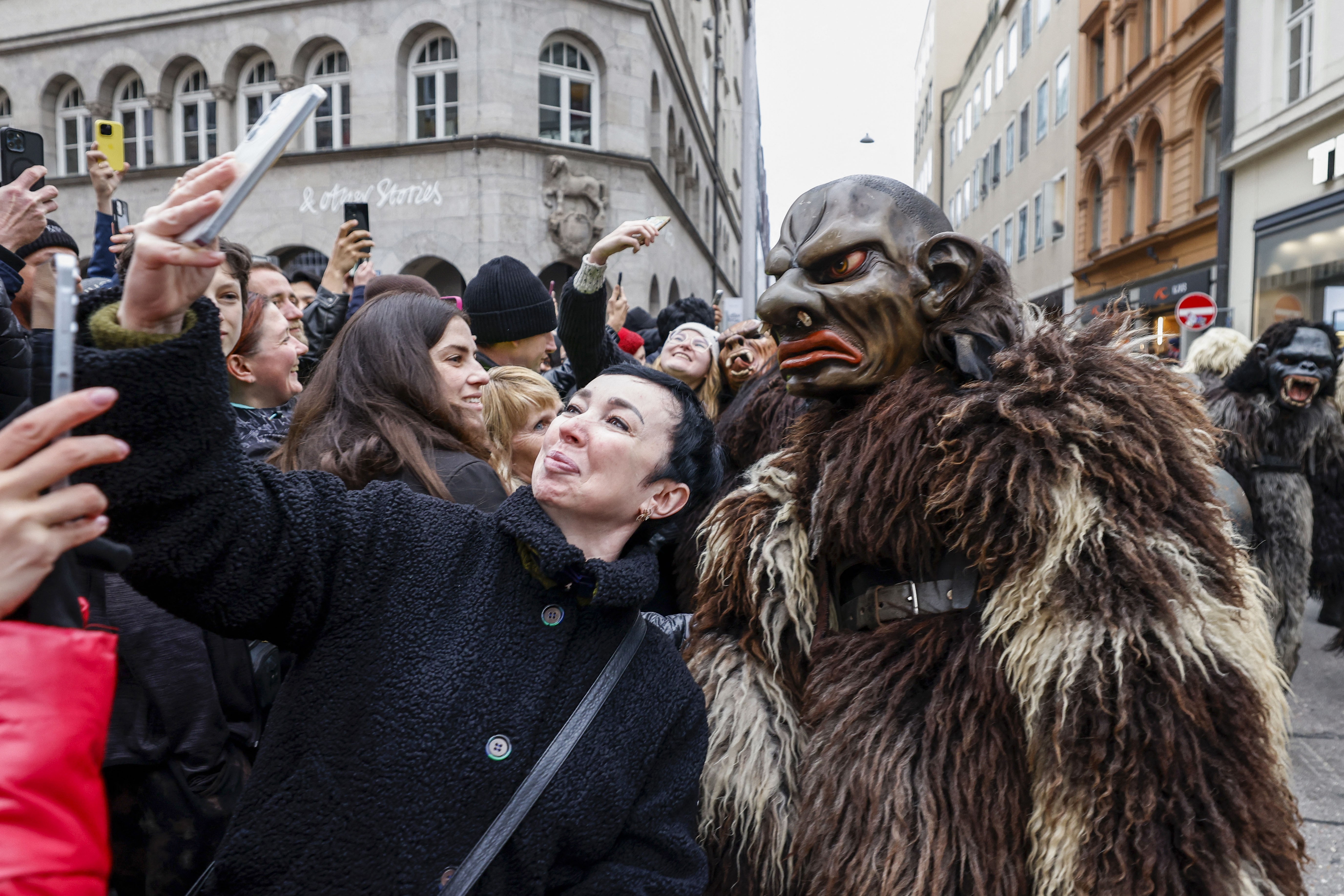 A spectator takes a selfie with a participant dressed as Krampus during a parade.