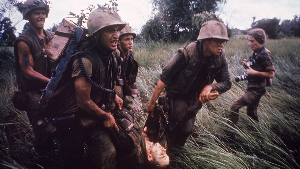 Marines recovering a dead comrade while under fire in South Vietnam. Photographer Catherine LeRoy holds cameras behind them.