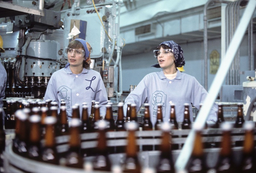 Actors Penny Marshall and Cindy Williams stand in costume in a fictional beer bottling plant.