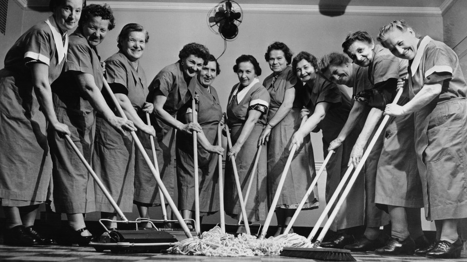 Women in maid uniforms smile at the camera while pushing mops.