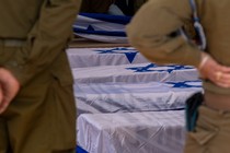 Soldiers looking solemnly at graves covered in Israeli flags