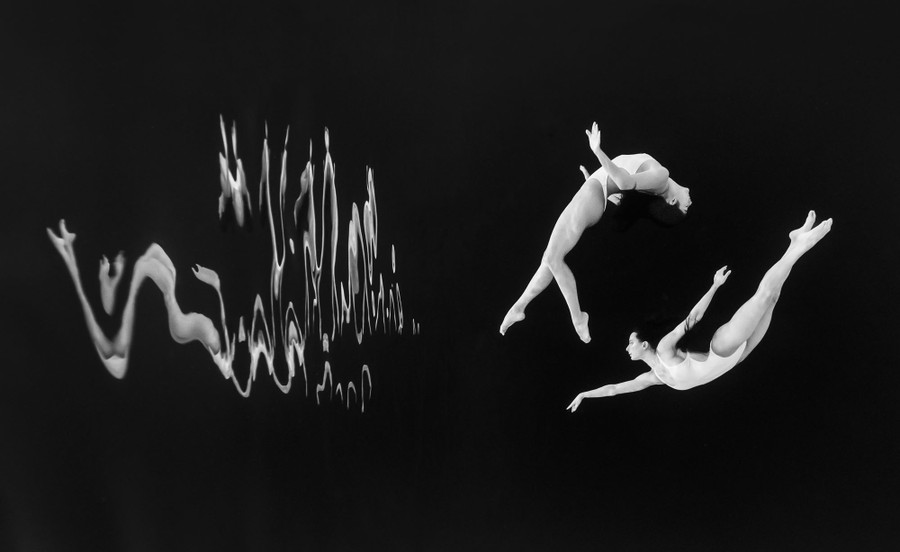 A sideways view of two swimmers performing underwater in a dark swimming pool