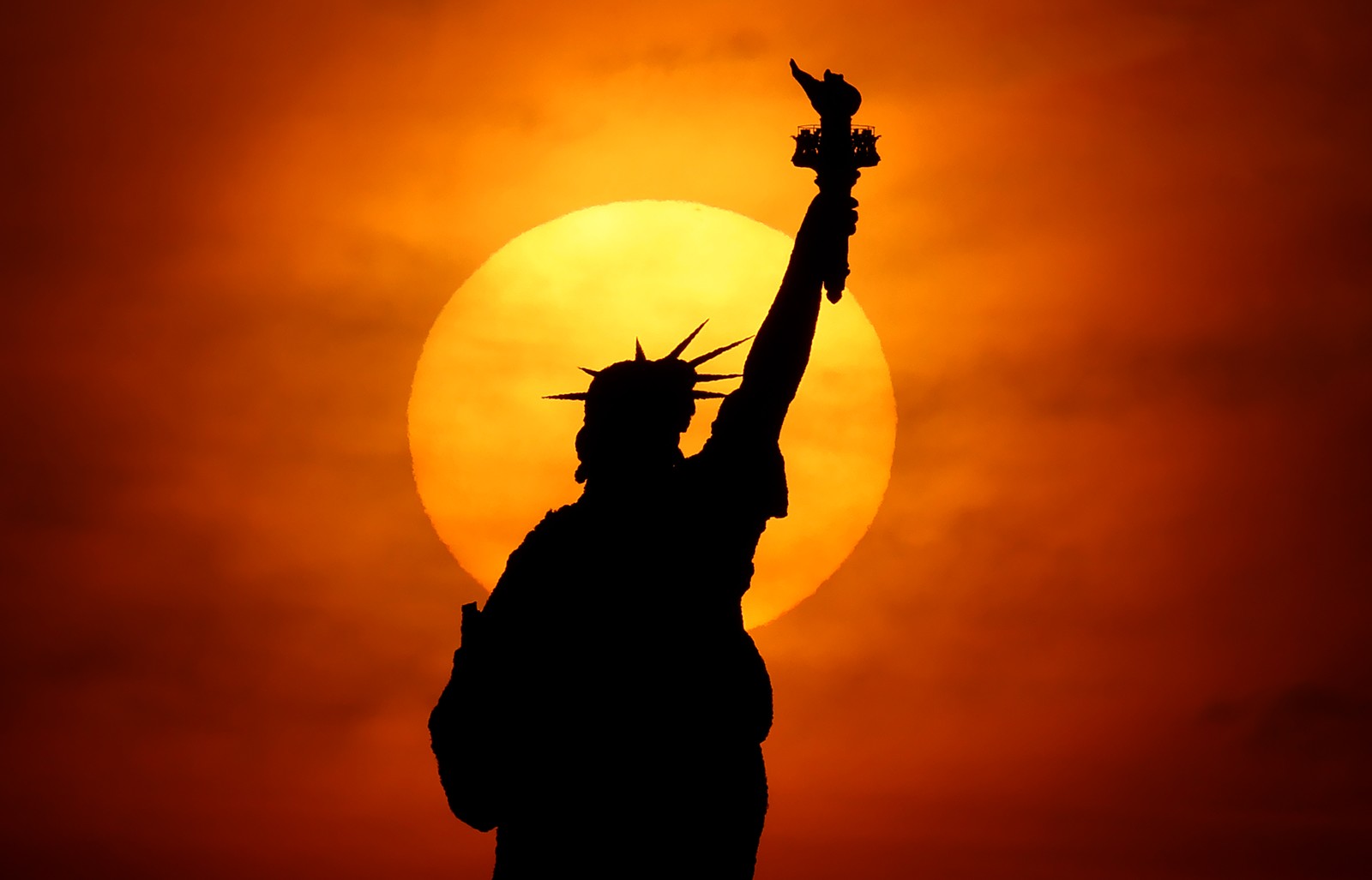 The sun rises behind the Statue of Liberty.