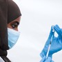 A woman wearing a blue mask and gloves pulls vaccine into a syringe.