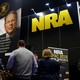 People in front of a booth with a picture of Wayne LaPierre and the NRA logo