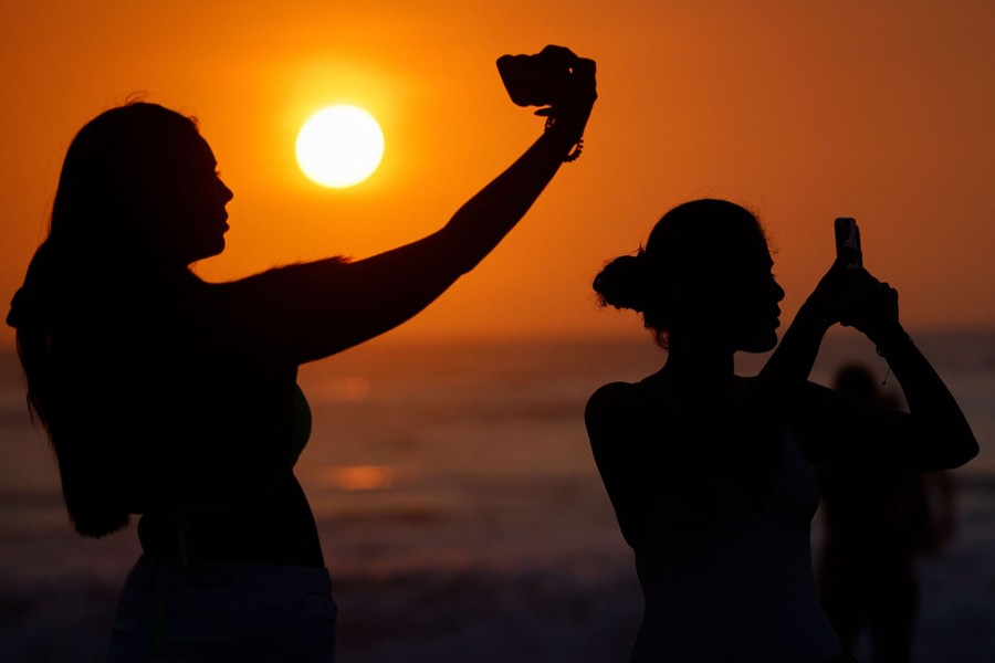 People use their mobile phones to take photos on a beach at sunset.
