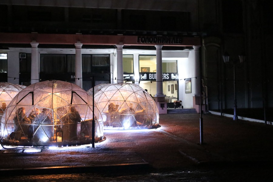 Café visitors sit in illuminated dome-shaped pavilions at night.