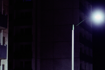 night photo of edge of building with balcony next to bright streetlight with pitch-black background