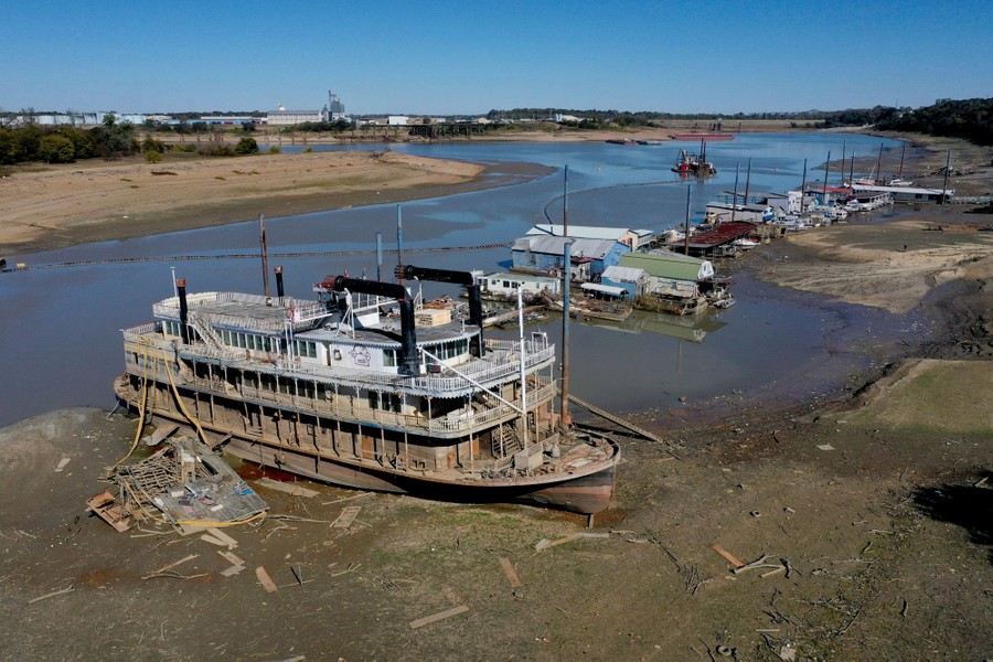 An elevated view of an old riverboat and several smaller boats grounded in mud, stranded by low river-water levels.