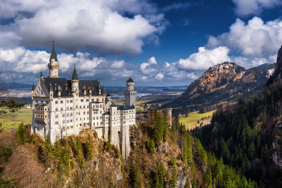 A view of a large hilltop castle, with an alpine valley visible in the distance.
