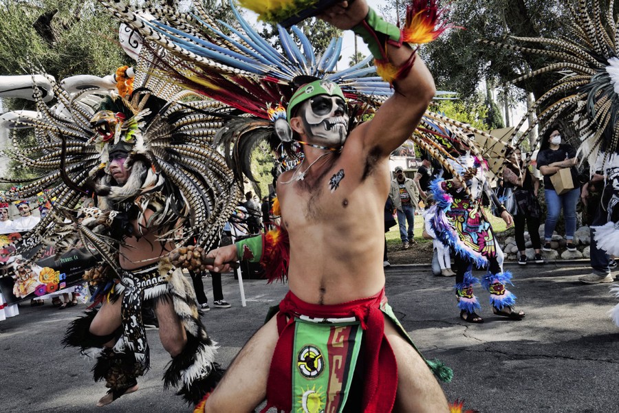 Performers in colorful feathery costumes dance.