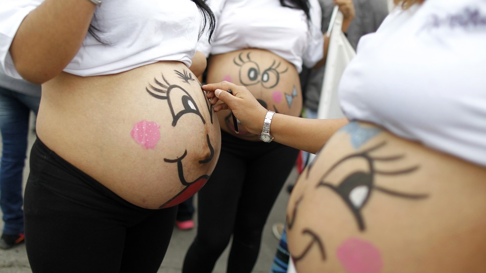 Pregnant women paint smiling faces on their bellies.