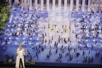An Apple speaker stands in front of a screen depicting people gathered in a town square