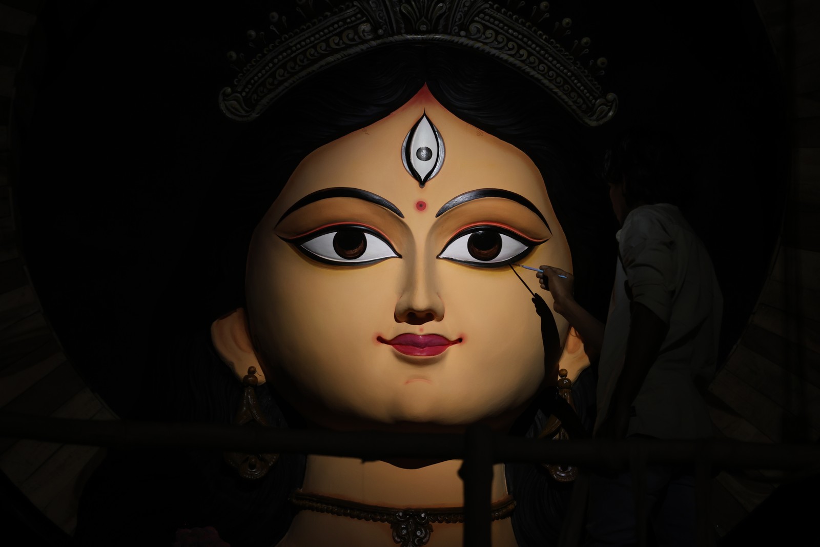 A person uses a paintbrush on the large head of a statue of a Hindu goddess.