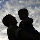 The silhouette of a father holding his son with a cloudy blue sky in the background