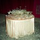 A table covered with a sparkling pink tablecloth is piled high with broken glassware and champagne flutes