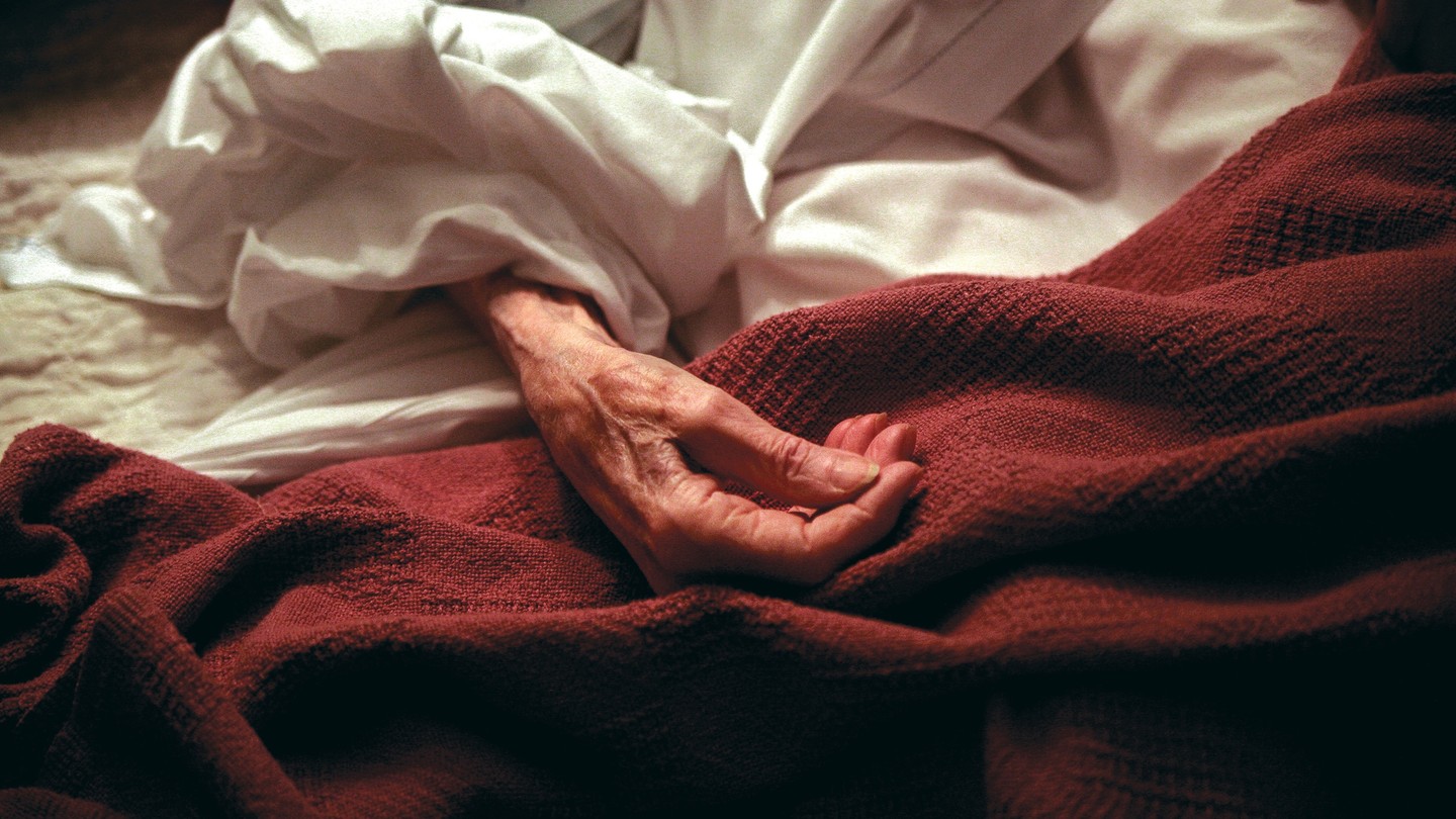 red blanket on hospital bed with an elderly hand on top