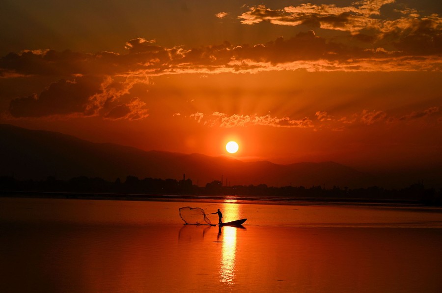 A person casts their net into a lake at sunset.