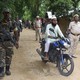 Indian security officers patrol a dirt road as a man rides past them on a motorcycle.